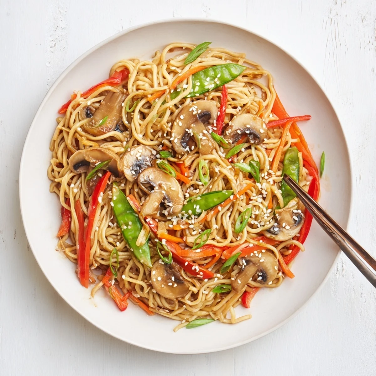 Steaming plate of garlic mushroom chow mein tossed with colorful vegetables and savory sesame sauce