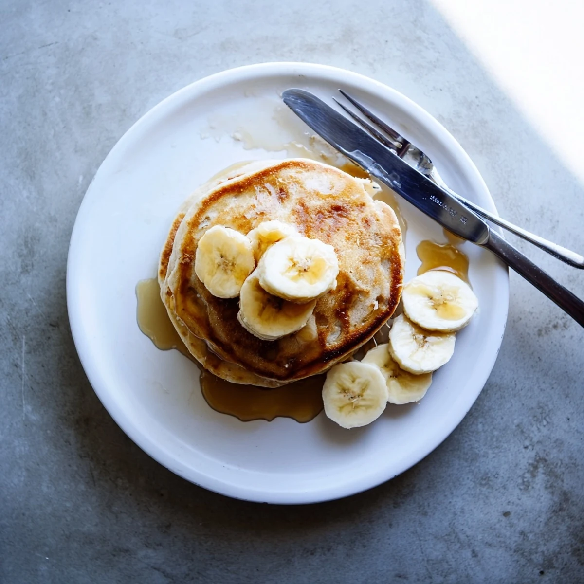 Protein-rich Greek yogurt banana pancakes stacked on a white plate with honey and sliced bananas