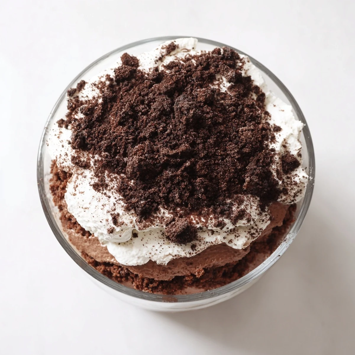 Glass trifle dish displaying layered keto dirt cake with chocolate pudding, whipped cream, and dark crumble topping