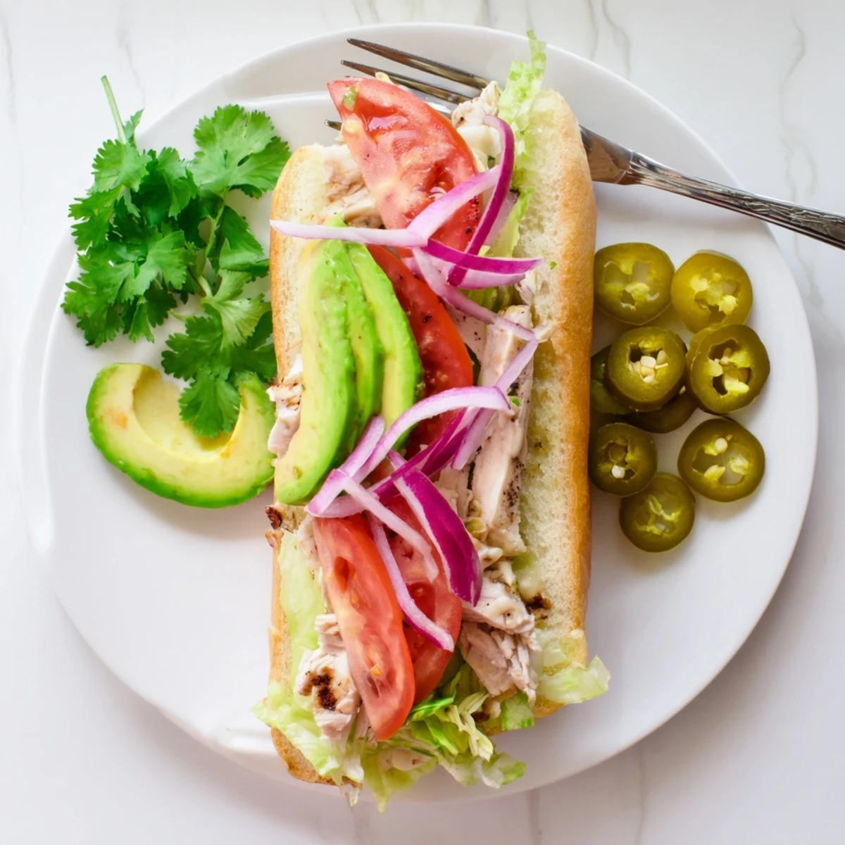 Golden Chicken Torta Sandwich stacked with marinated grilled chicken, creamy avocado, and zesty jalapeños on a toasted bolillo roll