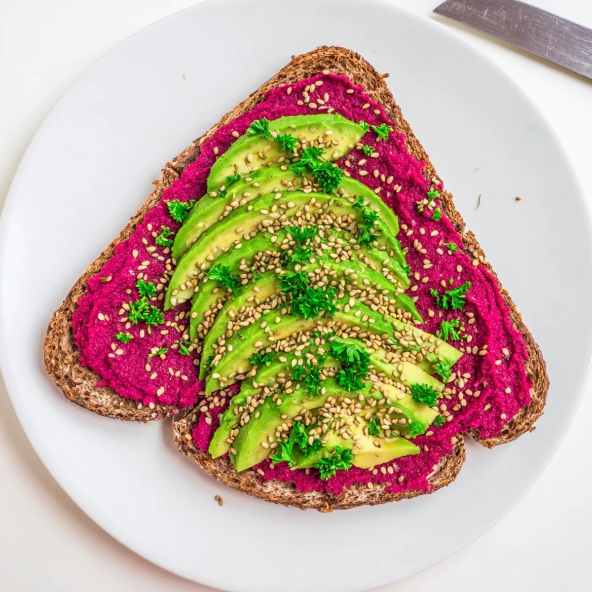 Open-faced toast layered with creamy avocado beet hummus sprinkled with sesame seeds