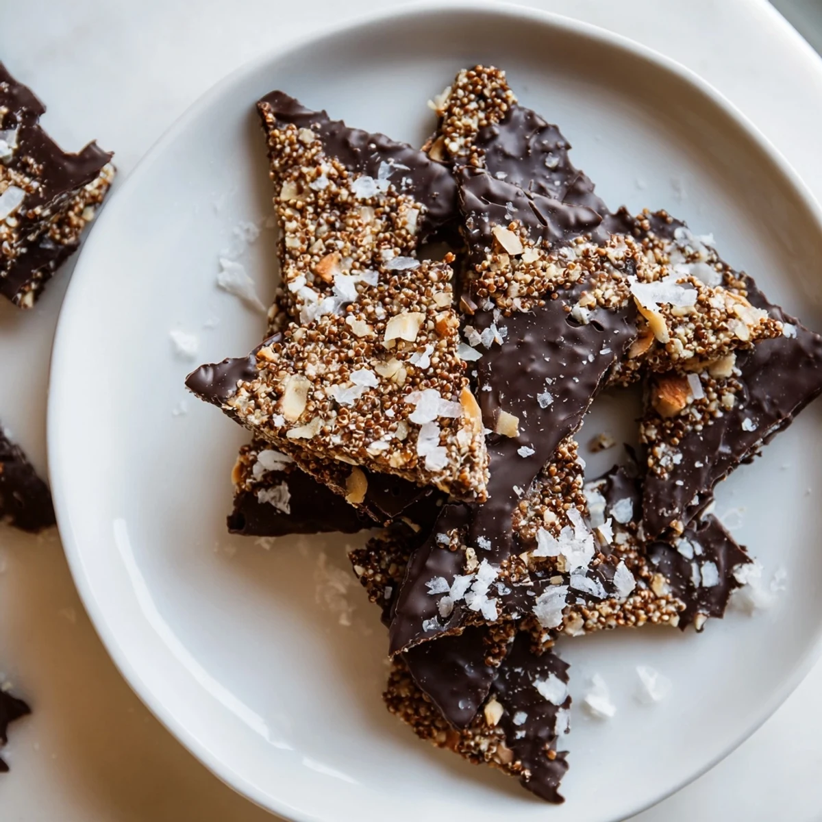 Golden dark chocolate quinoa crisps sprinkled with sea salt on a white plate