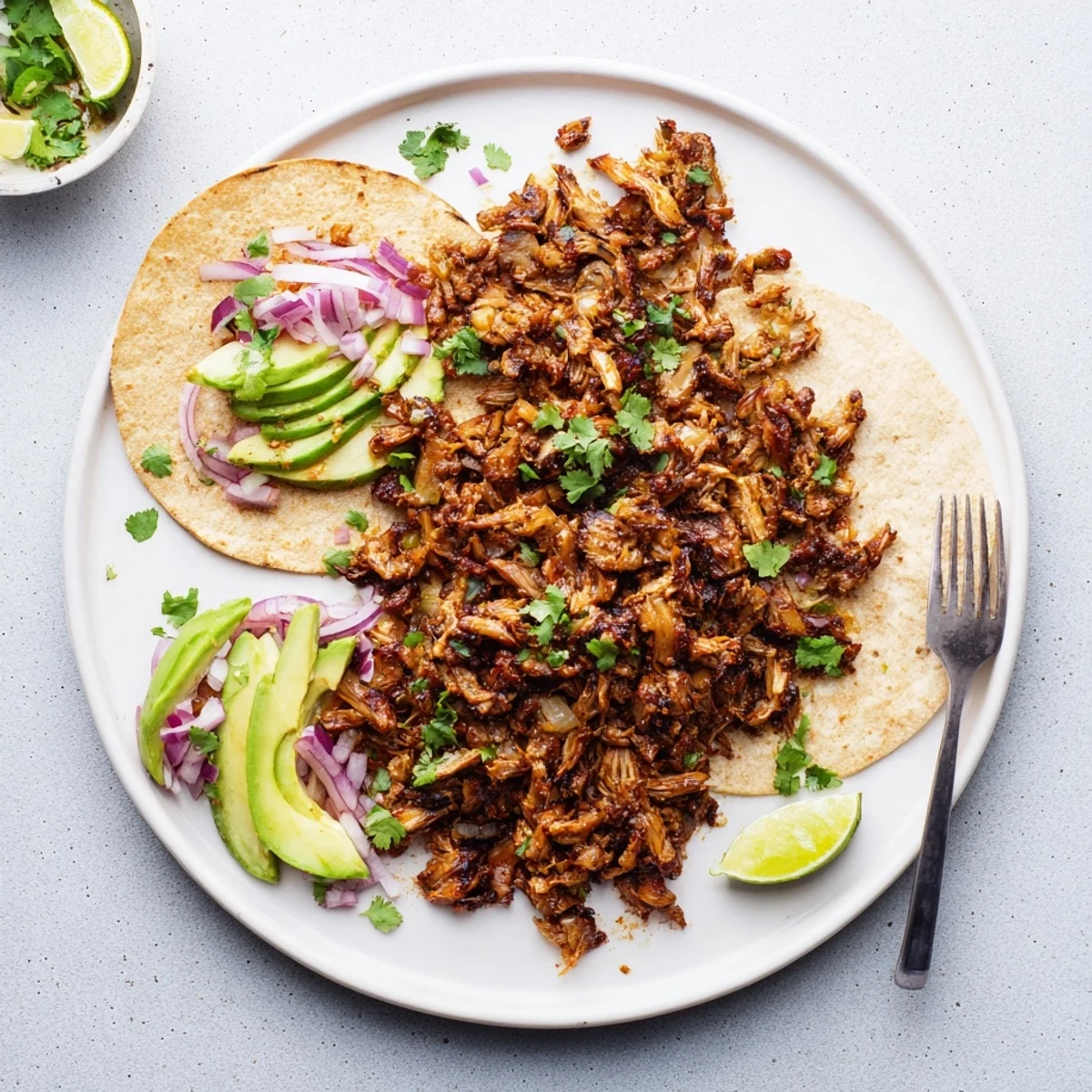 Golden brown vegan carnitas with shredded mushrooms nestled in warm corn tortillas and topped with fresh cilantro