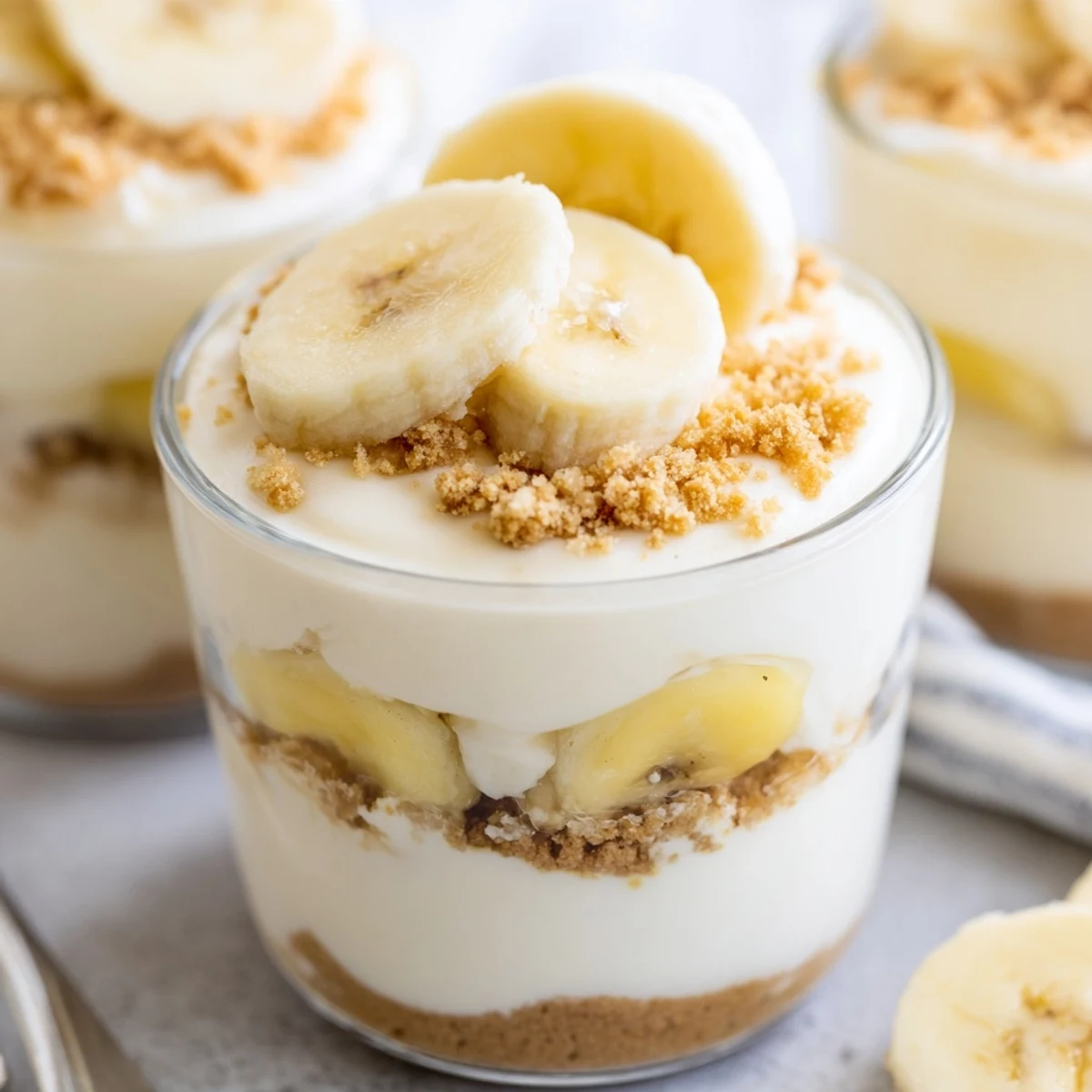 Individual no bake banana pudding cheesecake cups with layered banana slices and golden cookie crumb topping