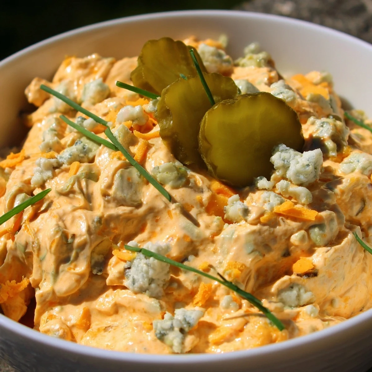 Creamy buffalo pickle dip in a rustic bowl surrounded by crunchy chips and fresh veggie sticks for dipping