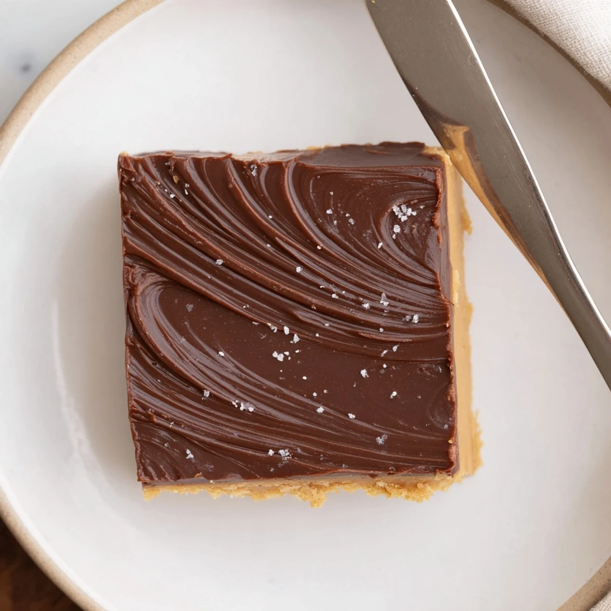 Hands lifting No Bake Peanut Butter Bars over parchment, rich nutty aroma.