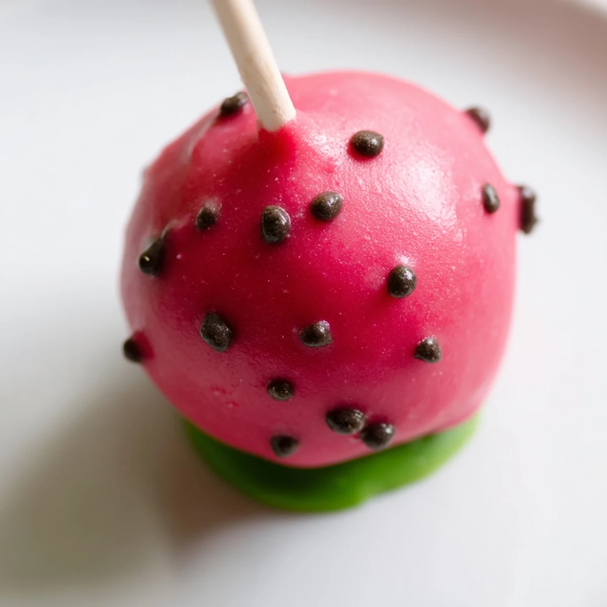 Hand holding a juicy watermelon cake pop on a stick with pink candy melt coating