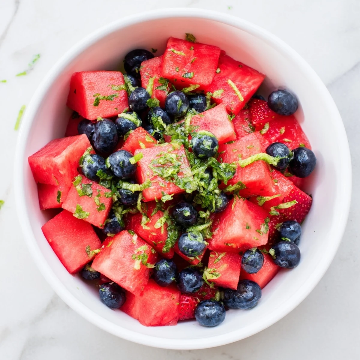 Refreshing watermelon dessert cubes with fresh strawberries, blueberries, and bright green mint topping served cold