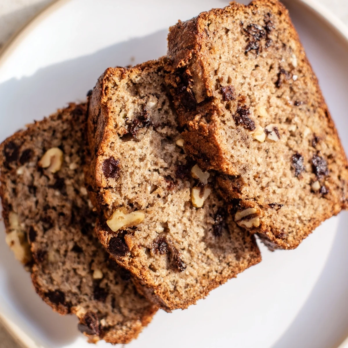 Golden protein banana bread slices topped with walnuts on a wooden cutting board