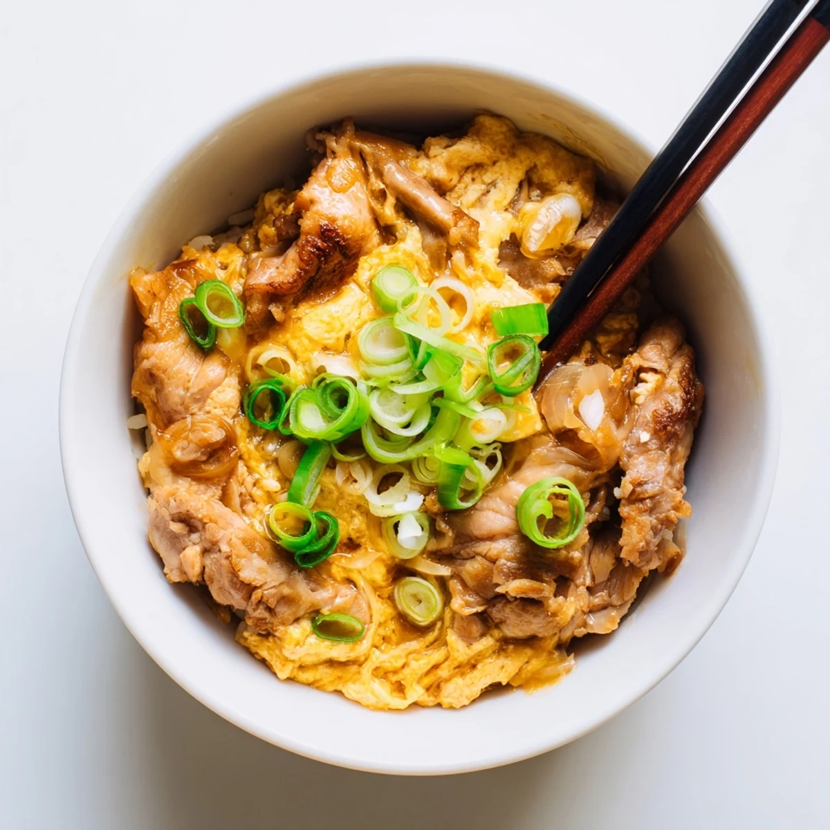 Comforting one-pot Oyakodon features simmered chicken onions and runny eggs garnished with fresh green onions