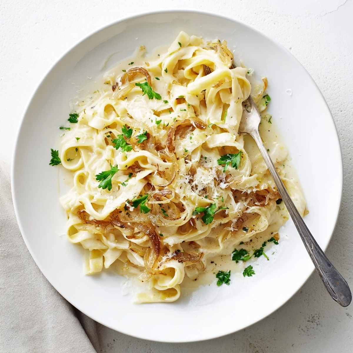 Steaming bowl of caramelized onion cream pasta garnished with fresh parsley and extra grated cheese