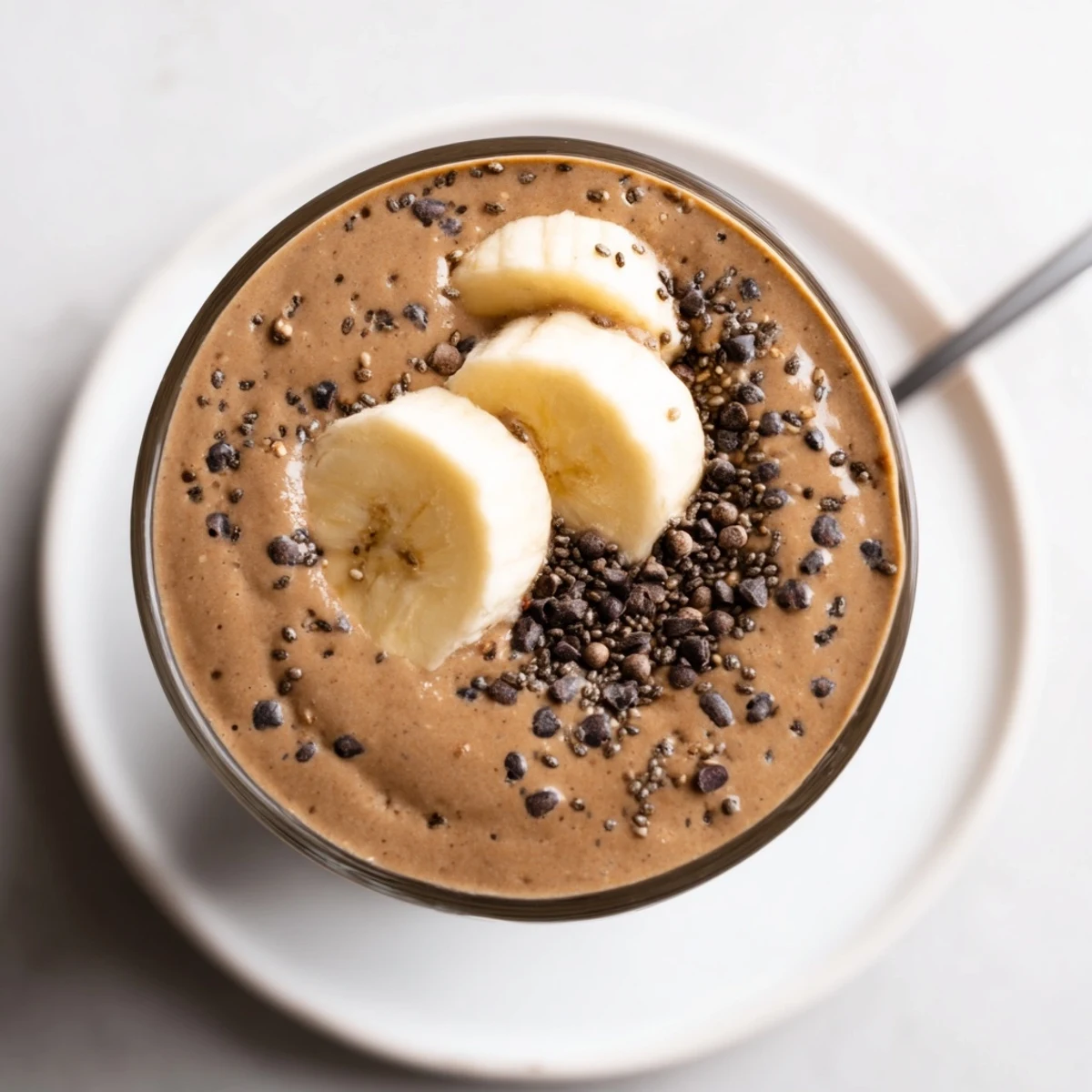Thick Raw Chocolate Banana Shake in glass with frothy top and straw