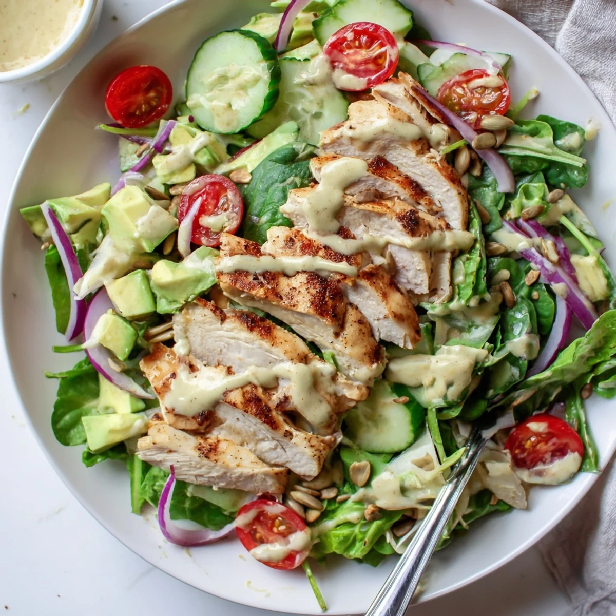 Tender grilled chicken breast drizzled with creamy honey mustard dressing over a fresh colorful salad in a bowl.