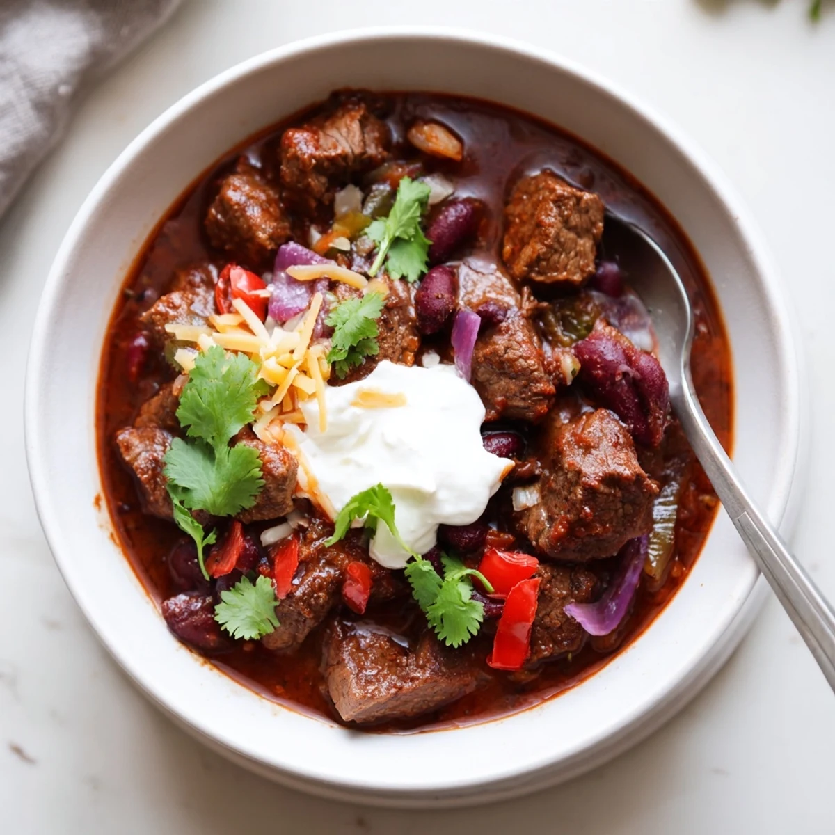 Thick beefy chili stew served with crusty bread, showcasing vibrant peppers and hearty kidney beans